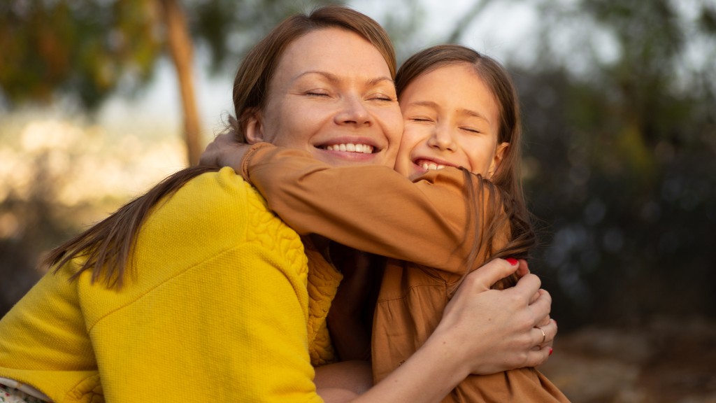 A mother and daughter sharing a warm hug outdoors in golden sunlight, both smiling with eyes closed