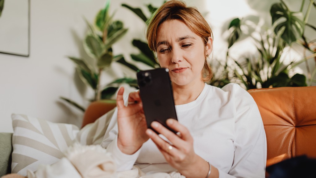 A woman sitting on a tan leather couch, calmly using her smartphone with green plants in the background