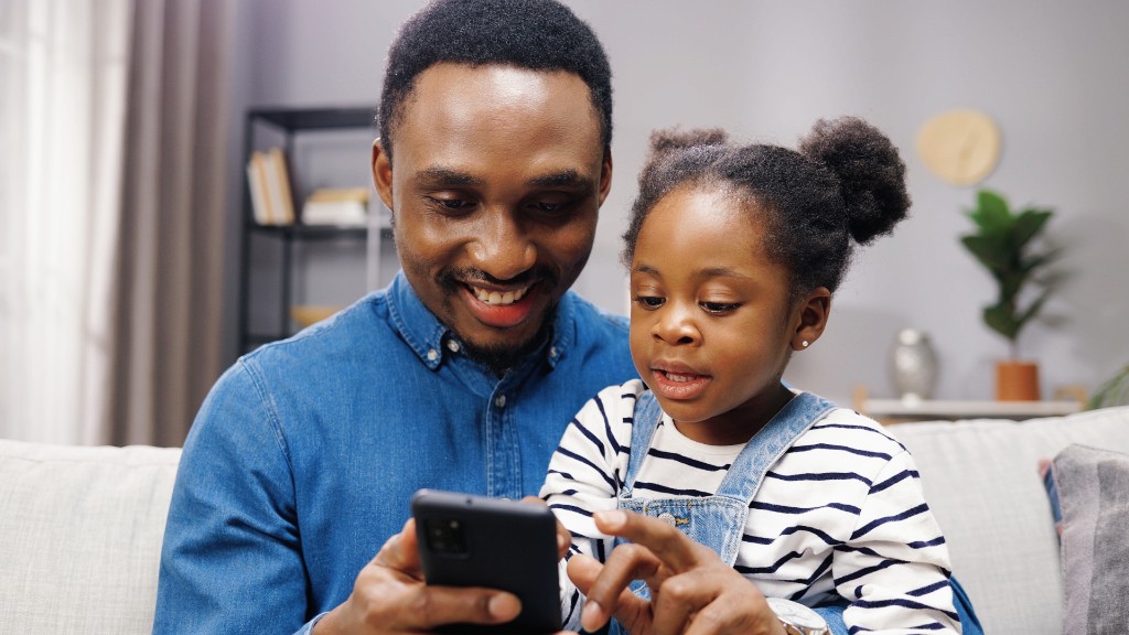 A father and young daughter sitting together on a couch, looking at a smartphone with focused curiosity