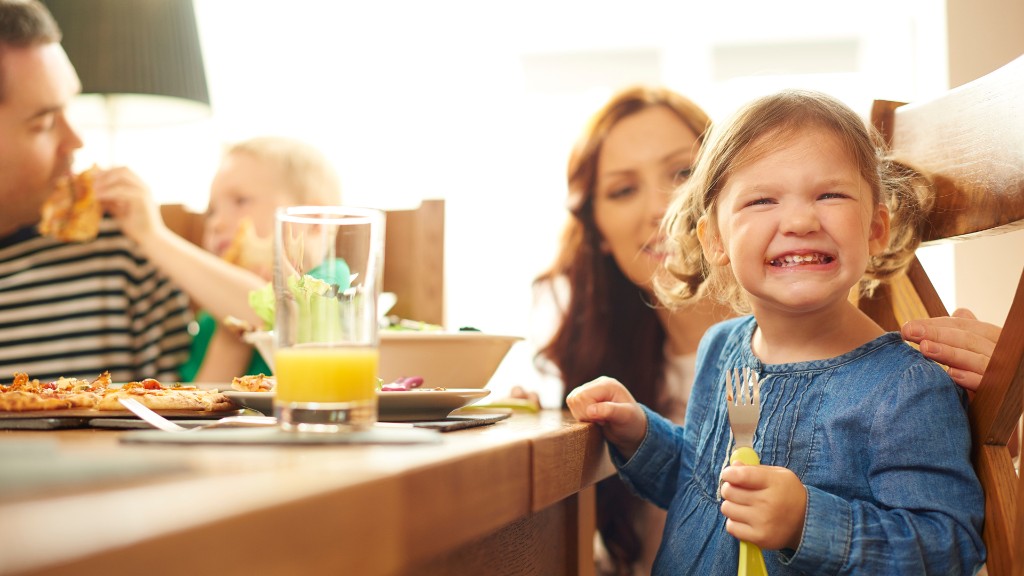 A young girl grimacing with eyes closed at the dinner table while her mother looks on with concern during a family meal