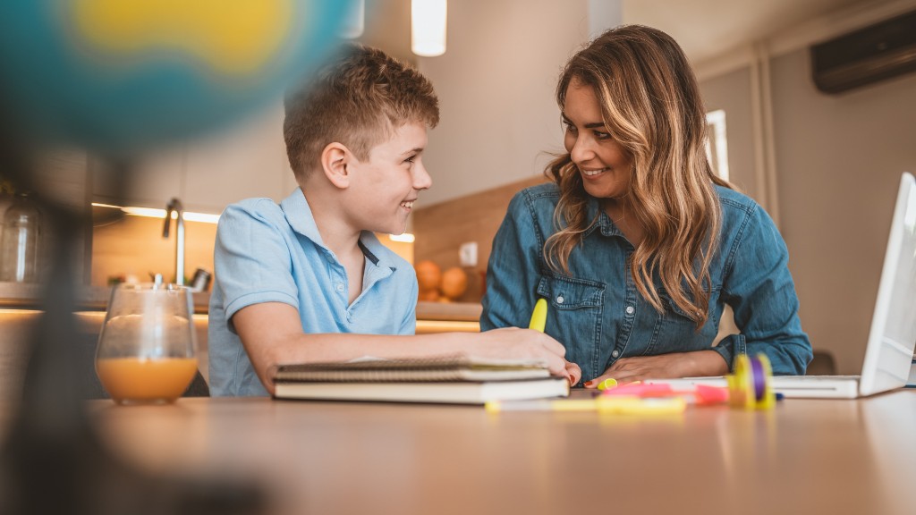 A woman and young boy smiling together at a kitchen table while working on homework with a laptop and highlighters