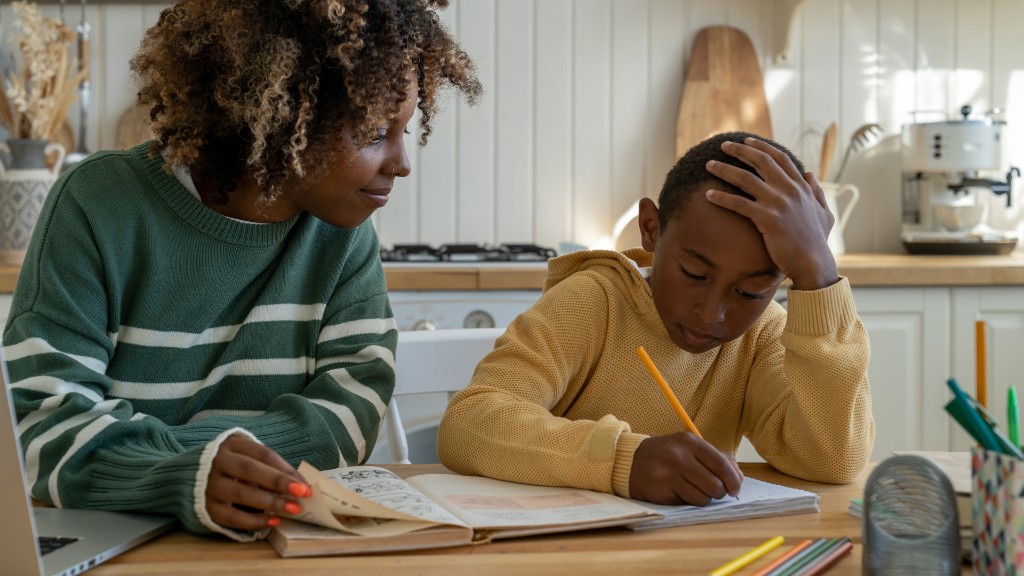A mother sitting beside her son at a kitchen table as he works on homework with a pencil