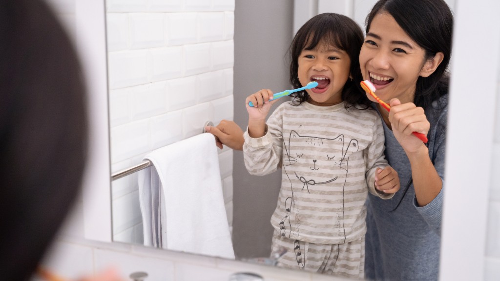 A mother and young daughter brushing their teeth together in front of a bathroom mirror