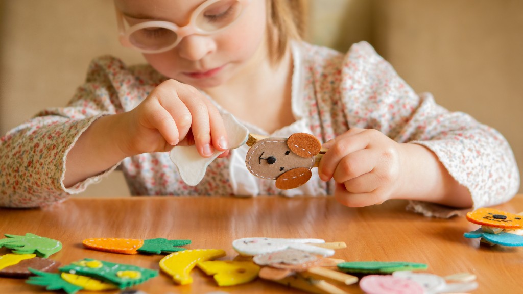 A young girl with pink glasses concentrating as she clips felt shapes with clothespins at a craft table