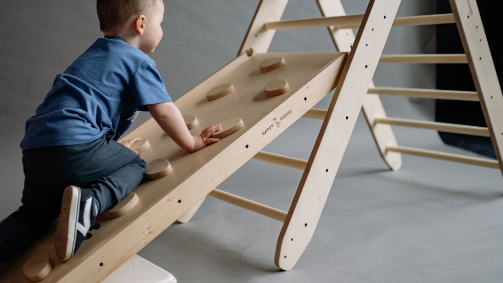 A young child climbing a wooden ramp attached to a Pikler triangle, gripping circular climbing holds