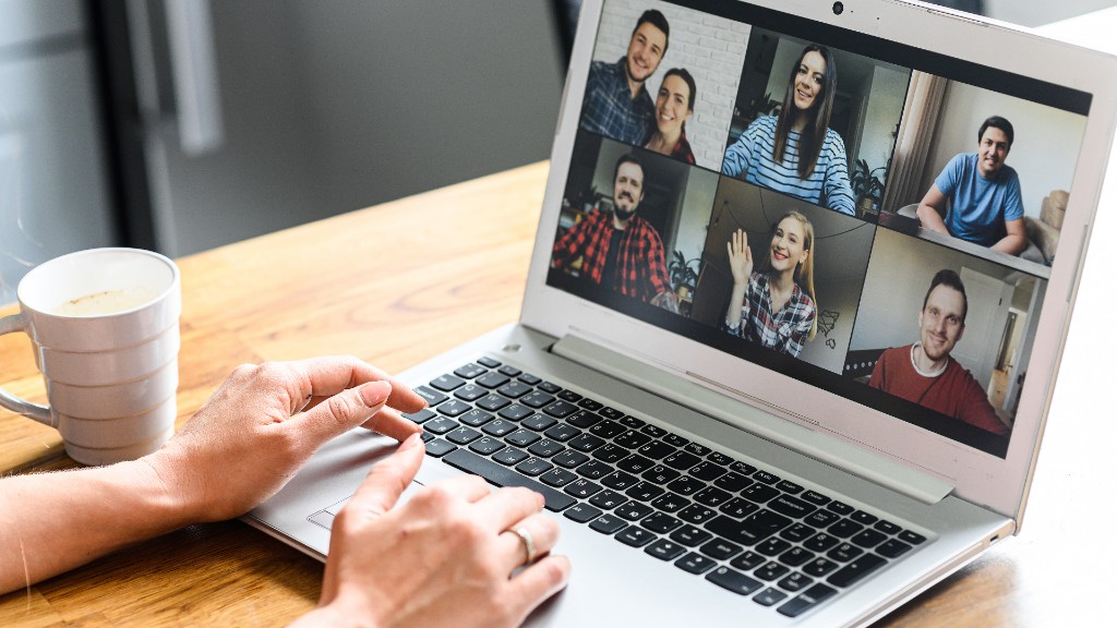 Overhead view of a laptop on a video call with six smiling participants and a coffee mug beside it