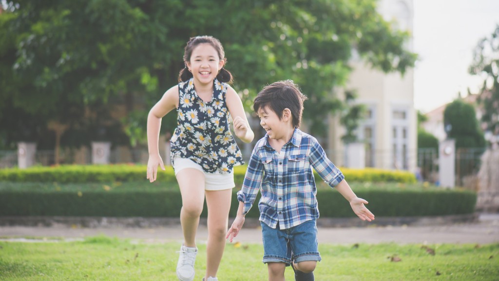 A girl and boy laughing as they run across a green lawn outdoors