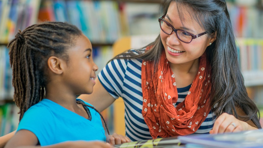 A teacher smiling at a young girl while they work together at a table in a library
