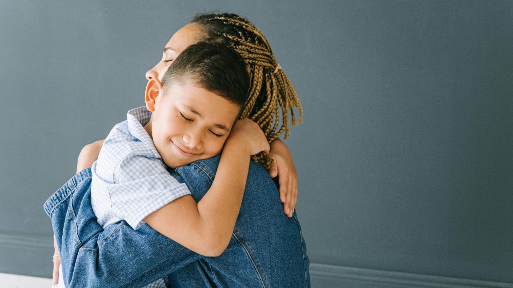 A young boy hugging a woman with braided hair, both with eyes closed in a calm embrace