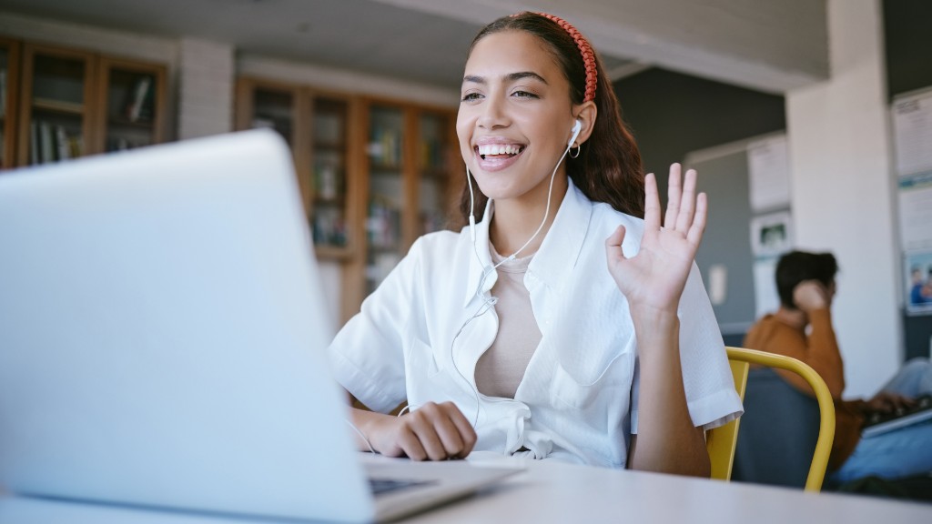 A smiling young woman waving during a video call on her laptop while wearing earbuds
