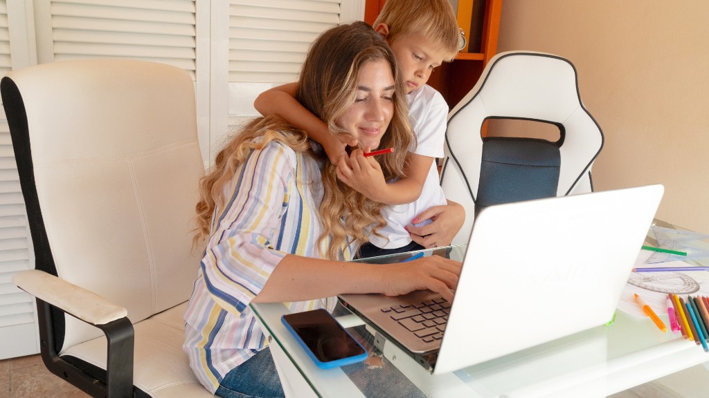 A young boy hugging his mother from behind while she works on a laptop at a home desk