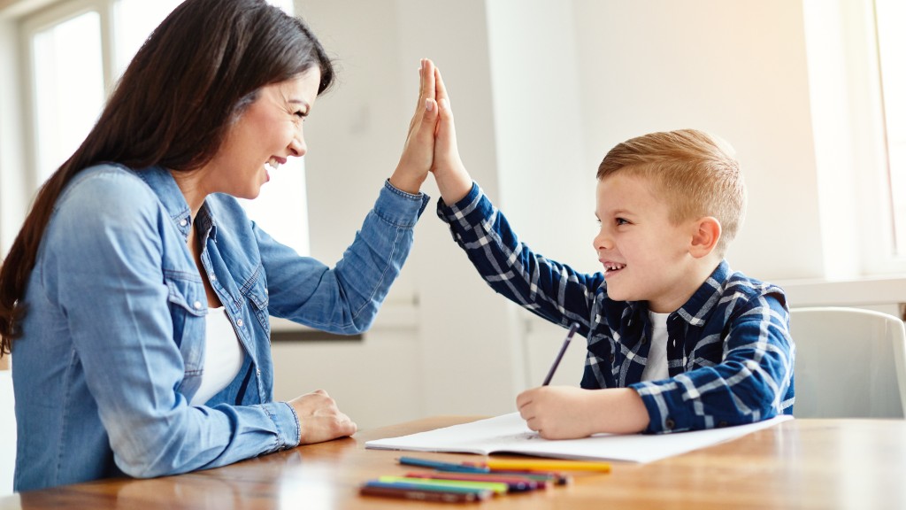 A woman and young boy smiling and giving each other a high-five over homework at a wooden table