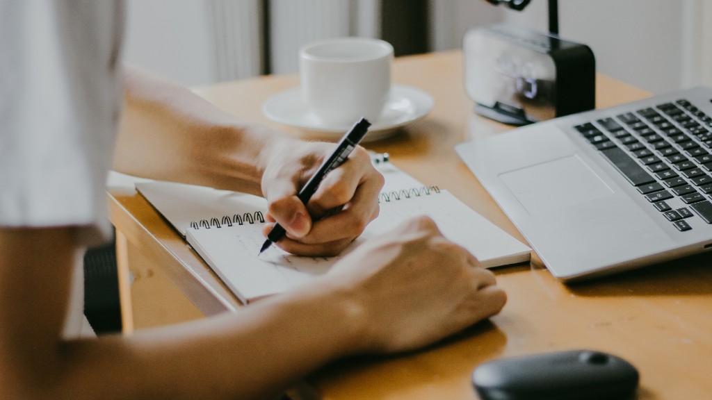 A person writing in a notebook at a desk with a laptop open beside them