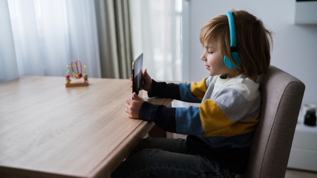 A young boy wearing blue noise-canceling headphones while using a tablet at a wooden table