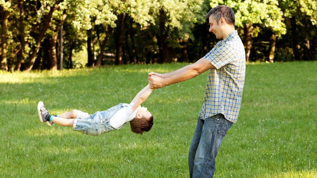 A father swinging his young son by the hands in a sunlit park, the boy flying horizontally through the air