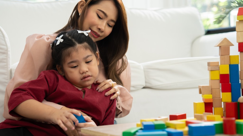 A mother with her arm around her daughter as they play with colorful wooden building blocks at a coffee table